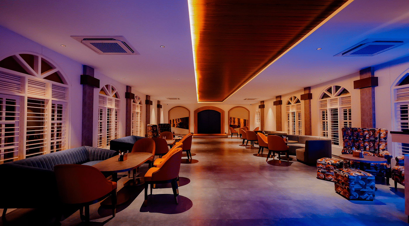 A long, dimly lit hallway with a bar area on the right, featuring colourful lighting and a modern design -  Nirantara Resort & Spa