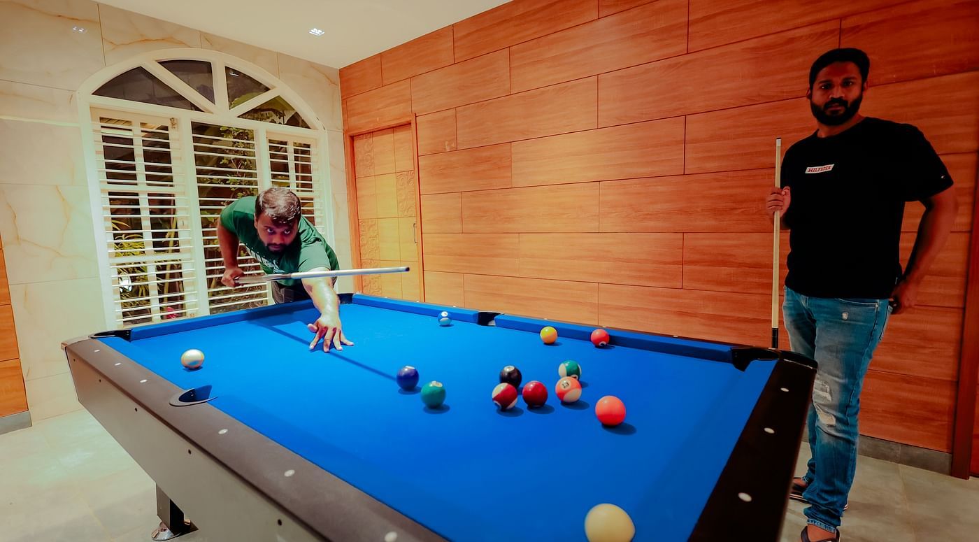 A person plays pool on a blue pool table in a room with brick walls and large windows - Nirantara Resort & Spa.