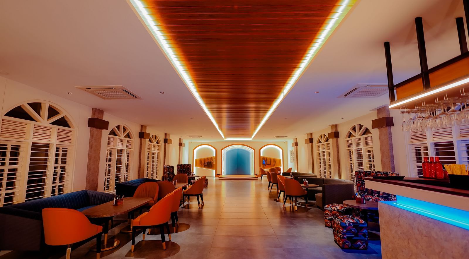 A long, brightly lit hallway with a bar area on the right, featuring colourful lighting and a modern design -  Nirantara Resort & Spa
