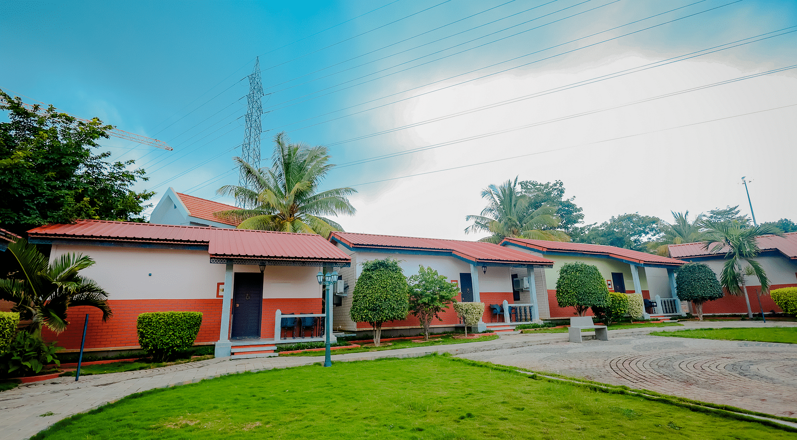 Exterior view of cottages with red roofs and green lawns at Nirantara Resort & Spa, Bengaluru, under a partly cloudy sky.