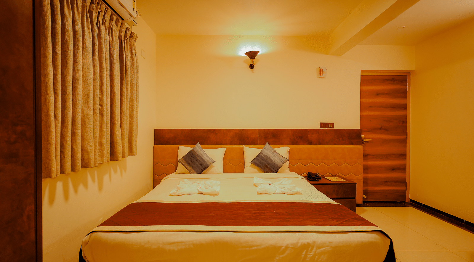 A comfortable bed in a room at Nirantara Resort & Spa, Bengaluru, with warm lighting and wooden furniture.