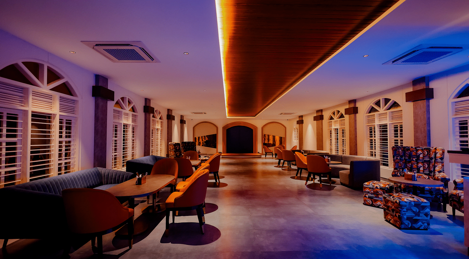A long, dimly lit hallway with a bar area on the right, featuring colourful lighting and a modern design -  Nirantara Resort & Spa