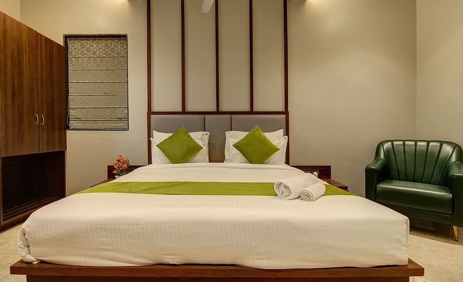 alt-text Double bed with a chair next to it inside Luxury Suite - Fortune House, Magarpatta