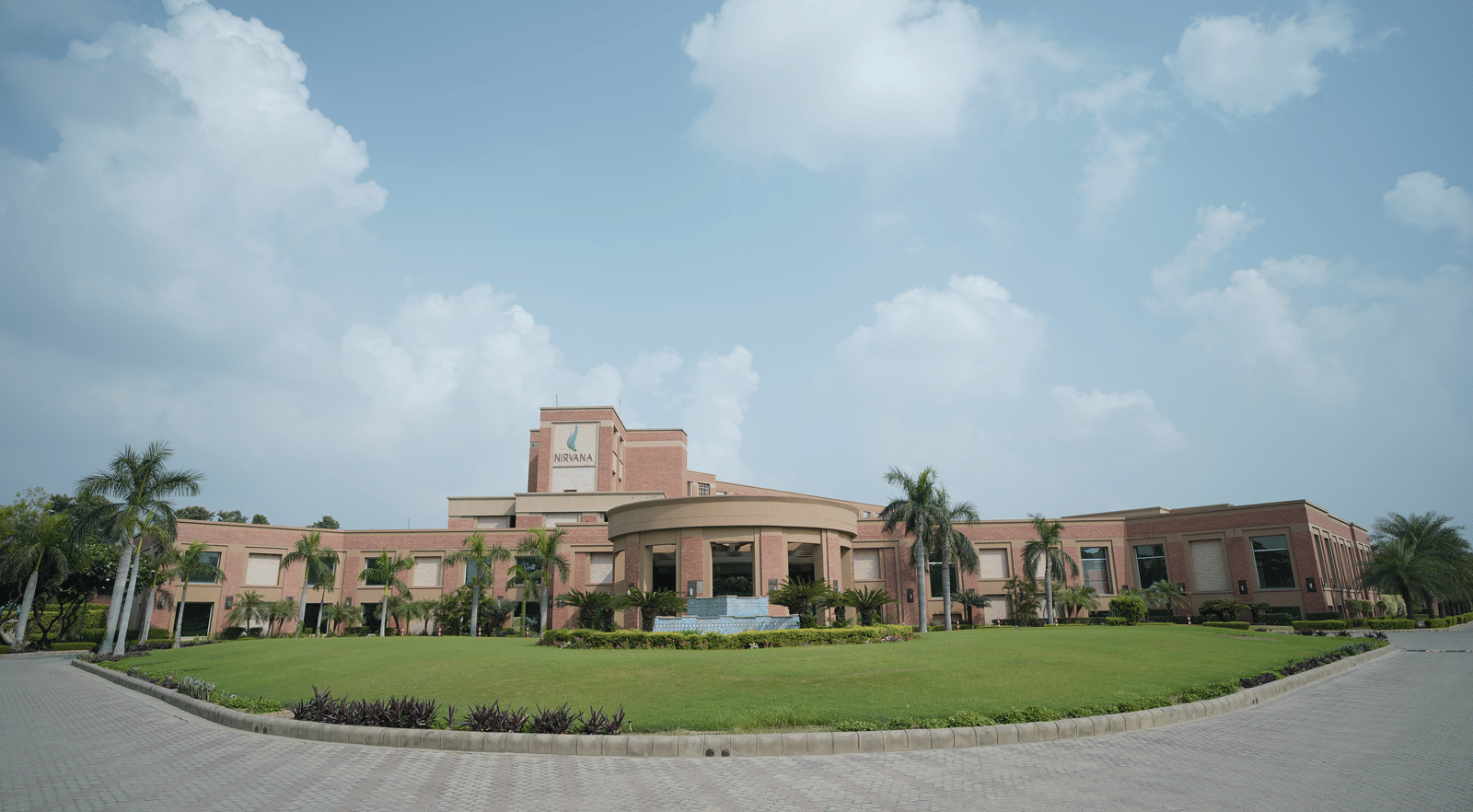 Exterior panoramic view of Nirvana Luxury Hotel, Ludhiana   - one of the best Wedding Halls in Ludhiana, during the day with a pathway and a manicured garden in view.