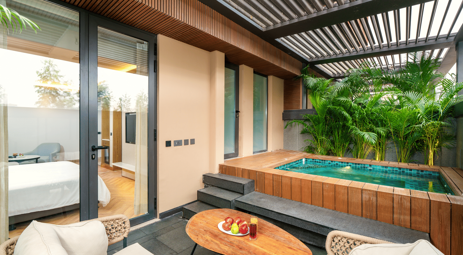 Nirvana Rooms with Plunge Pool (Ludhiana Hotel Room) at Nirvana Luxury Hotel, Ludhiana, features a private plunge pool surrounded by lush greenery, a cosy outdoor seating area with a wooden table, and direct access to the villa's interior.