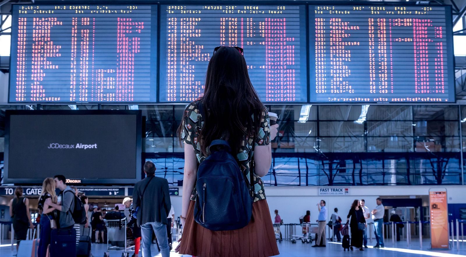 A close up of a women looking at the flight schedule in an airport with other people walking below it.
