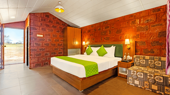 Nature Trails Kundalika – Deluxe room with king bed, green accents, and red brick wall decor.