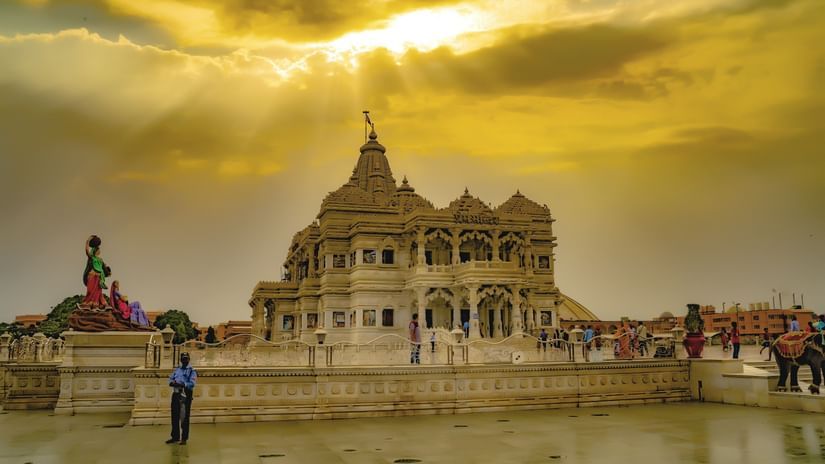 Stunning temple under a dramatic golden sky with sun rays shining through clouds, featuring intricate carvings, statues, visitors, and a polished courtyard.