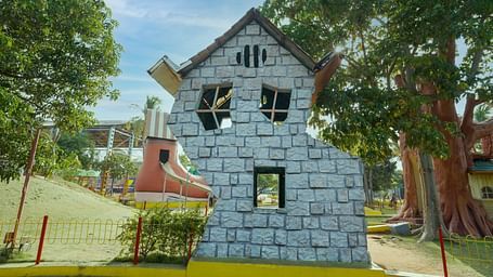 A playful, two-storied house facade built at MGM Dizzee World featuring stone blocks, set against a backdrop of trees and a bright sky.