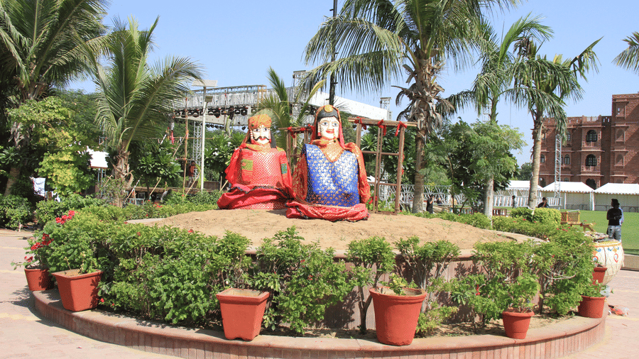 2 large traditional figures, on a raised garden bed surrounded by potted plants and palm trees at Garh Govind.