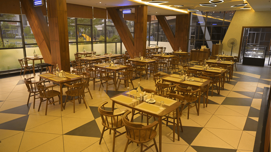 A wide view of a restaurant interior featuring wooden support beams and numerous dining sets at Hotel Sonar Bangla, Mayapur.