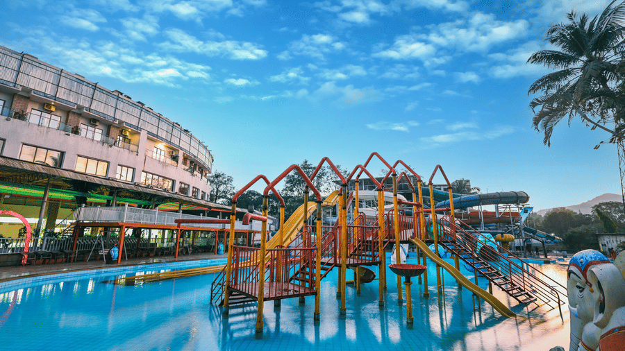 Expansive view of the water park featuring multiple themed structures, slides, and pools, with the resort building visible behind the water features at Kumar Resort by Turtle.