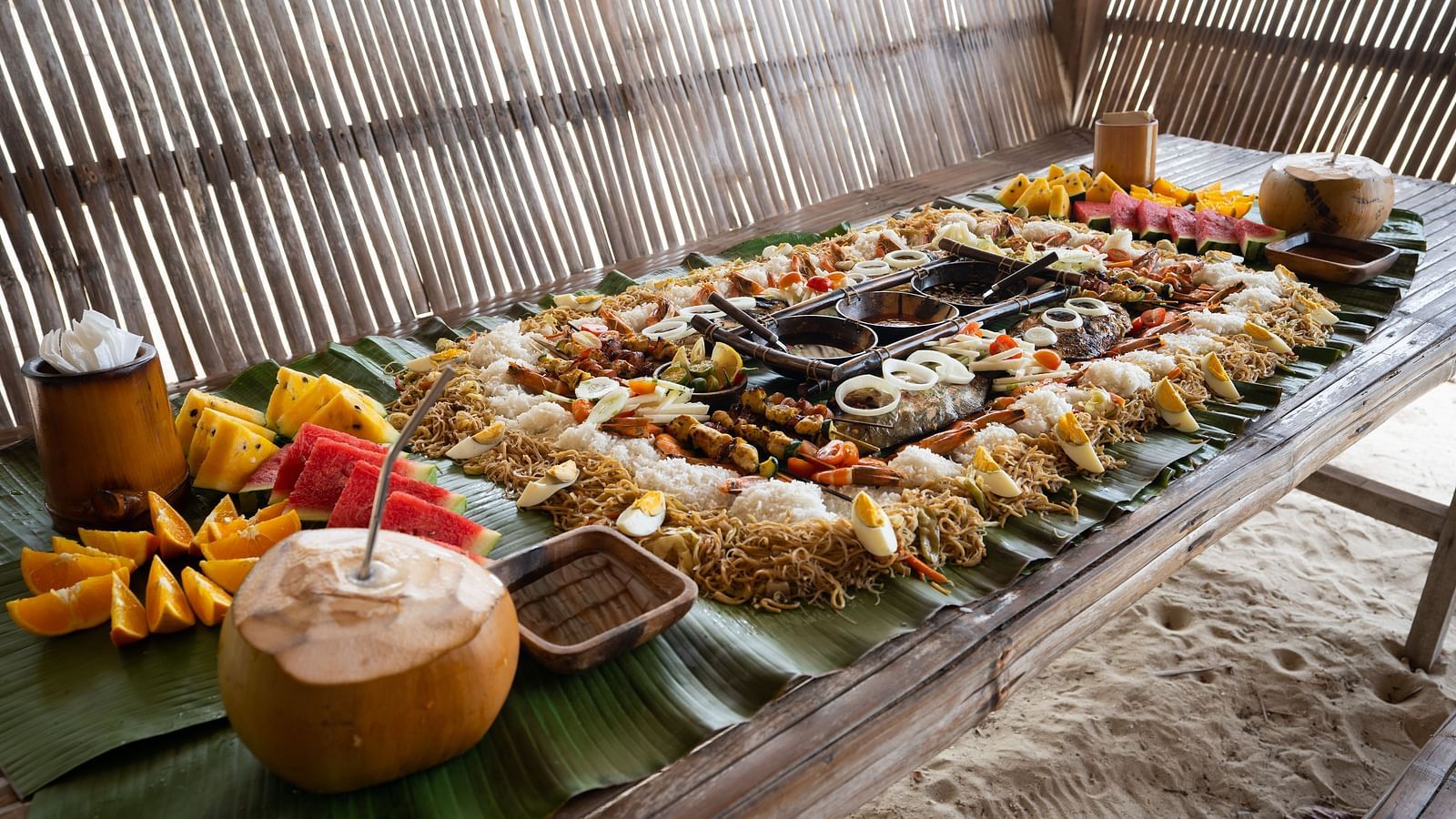 Spread of fruits, rice, tender coconut and local dishes arranged on a bamboo table at Flower Island Resort.