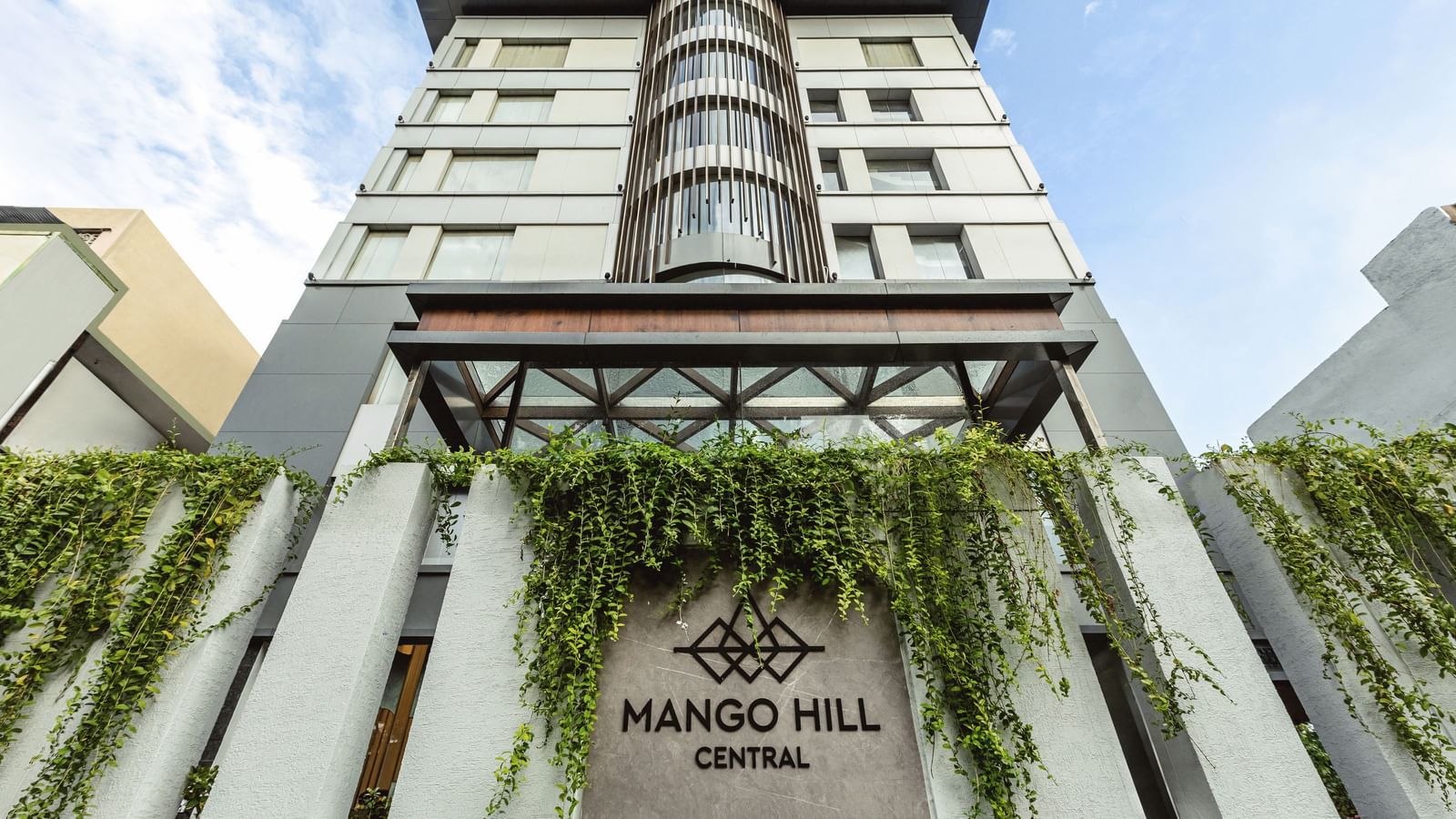 A straight-on exterior view of Mango Hill Central, Chennai, showing the multi-story building facade and the hotel name on the wall.