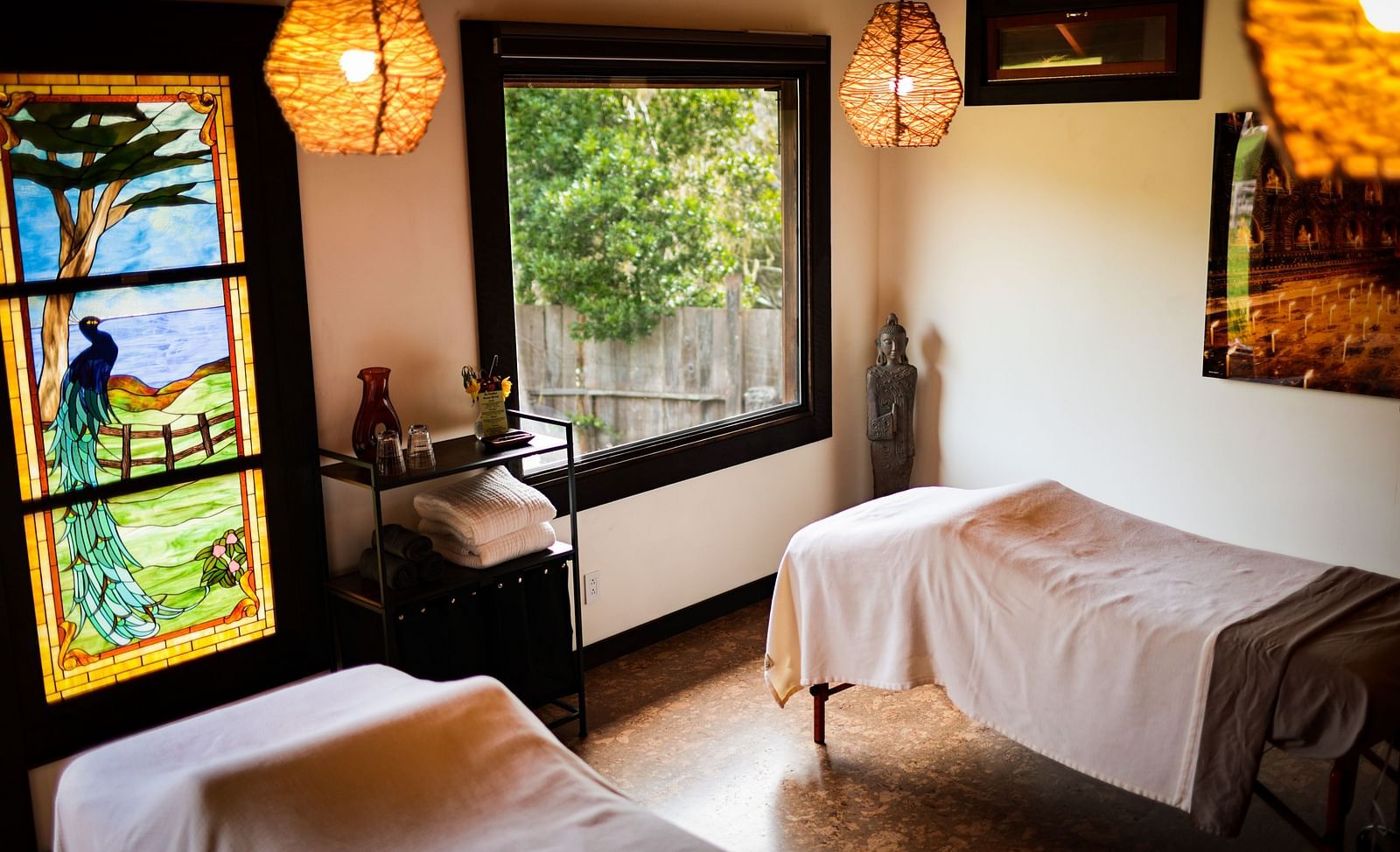 A massage room with soft lighting, white linens, and a window overlooking lush greenery - Brewery Gulch Inn & Spa