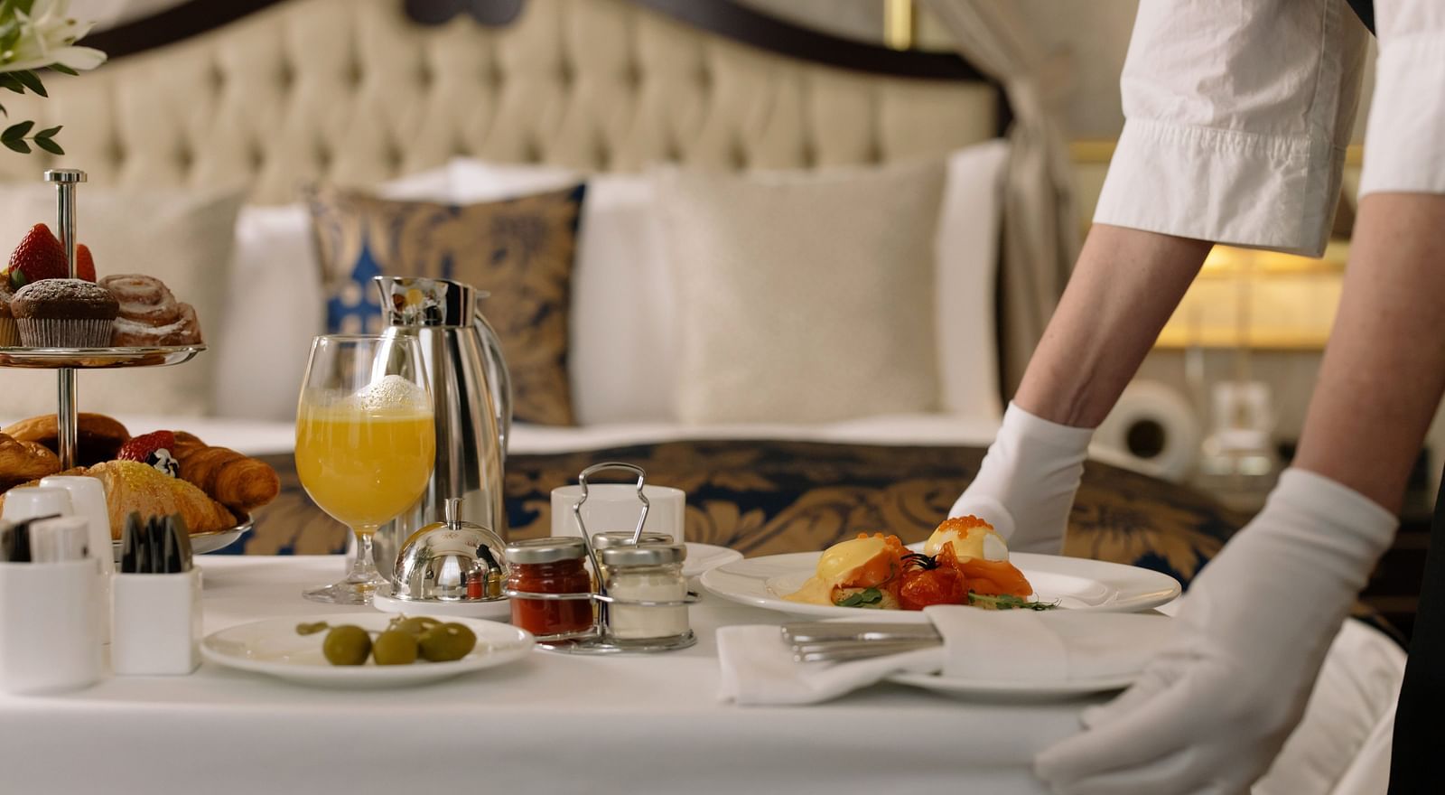 A room service attendant serving breakfast with eggs and pastries on a bed