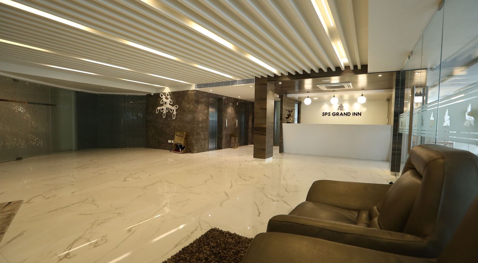 A spacious, well-lit lobby area with modern ceiling lights, light-coloured flooring, and comfortable lounge seating - TGI SPS Grand, Coimbatore
