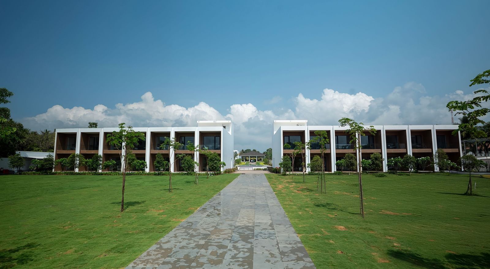  A lush green lawn at The Shore Trishvam, Pondicherry divided by a pathway in the middle with a clear blue sky in the background.