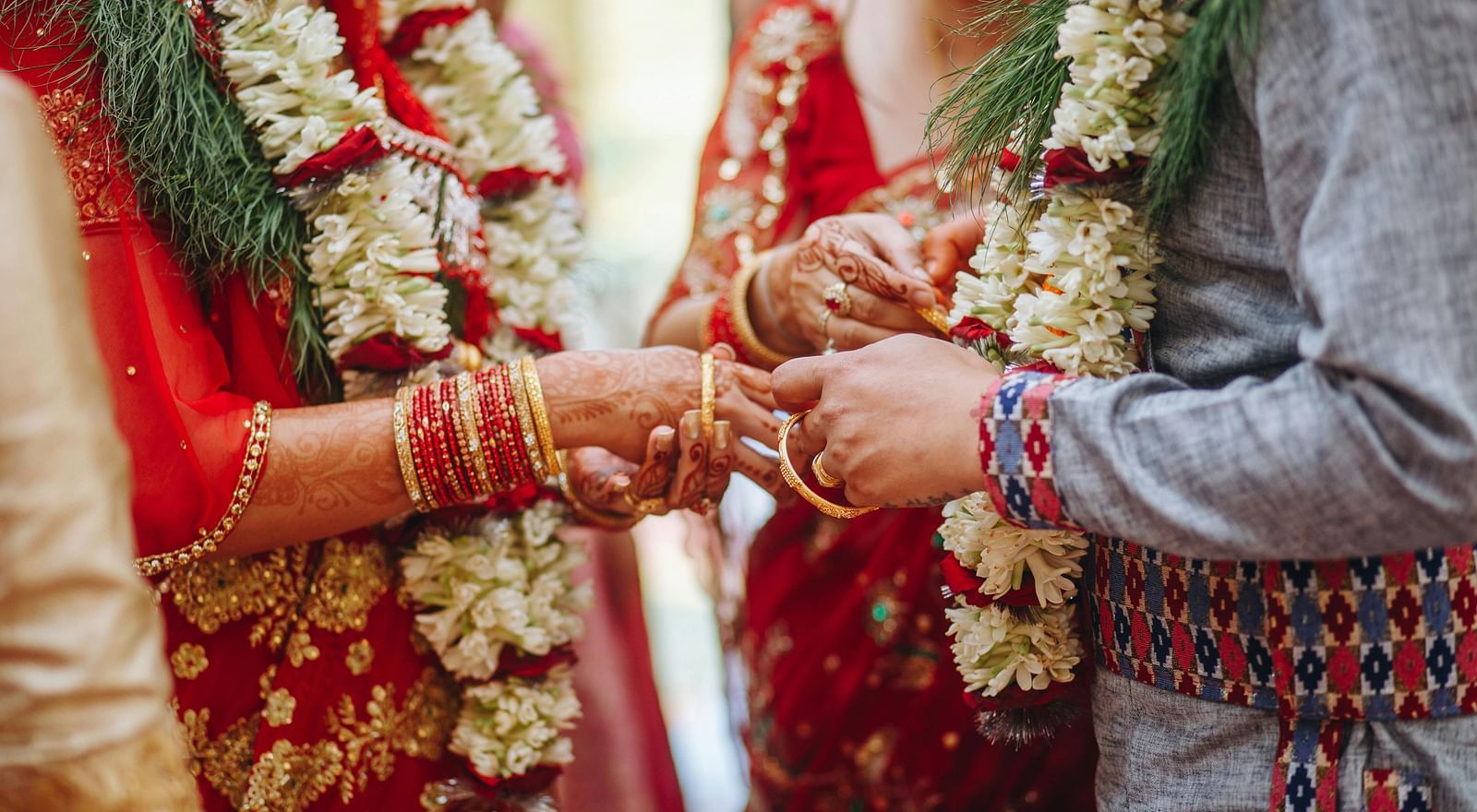 a couple wearing flower garlands exchanging rings with people around them