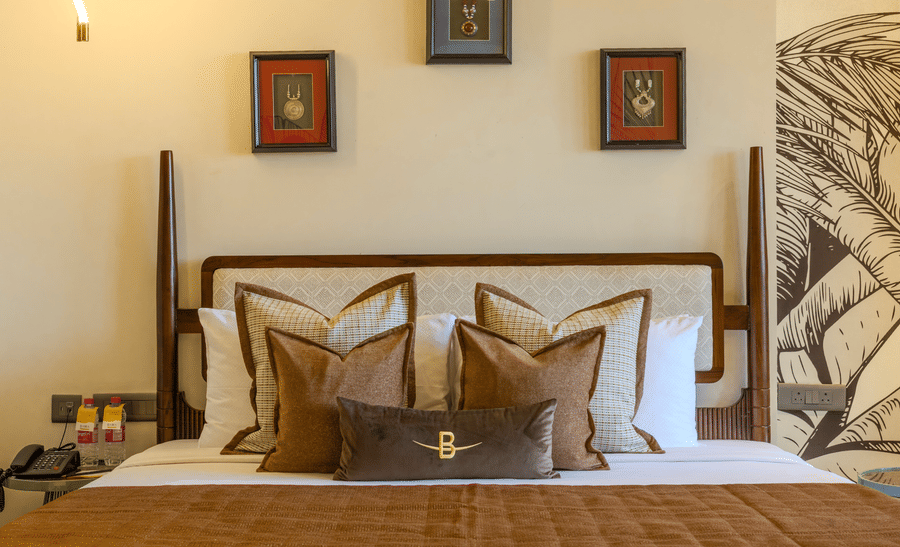 King size bed with layered decorative cushions, ambient bedside lighting and framed wall art at Hotel Bawa, Udaipur.