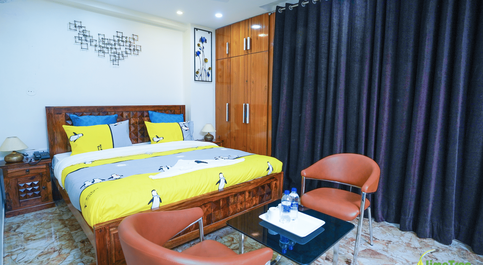 An image of a bedroom with a double size bed, a seating area with chairs and tables, a wardrobe, and a bedside table - Lime Tree Hotel Near 32nd Avenue