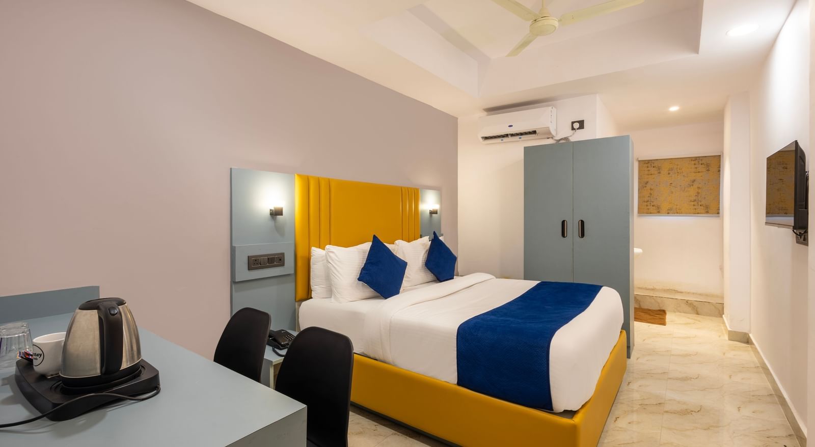 Side view of a Deluxe Room with a bed, blue and white bedding, a yellow headboard, and a desk area - Beestay Hotels Financial District, Hyderabad 
