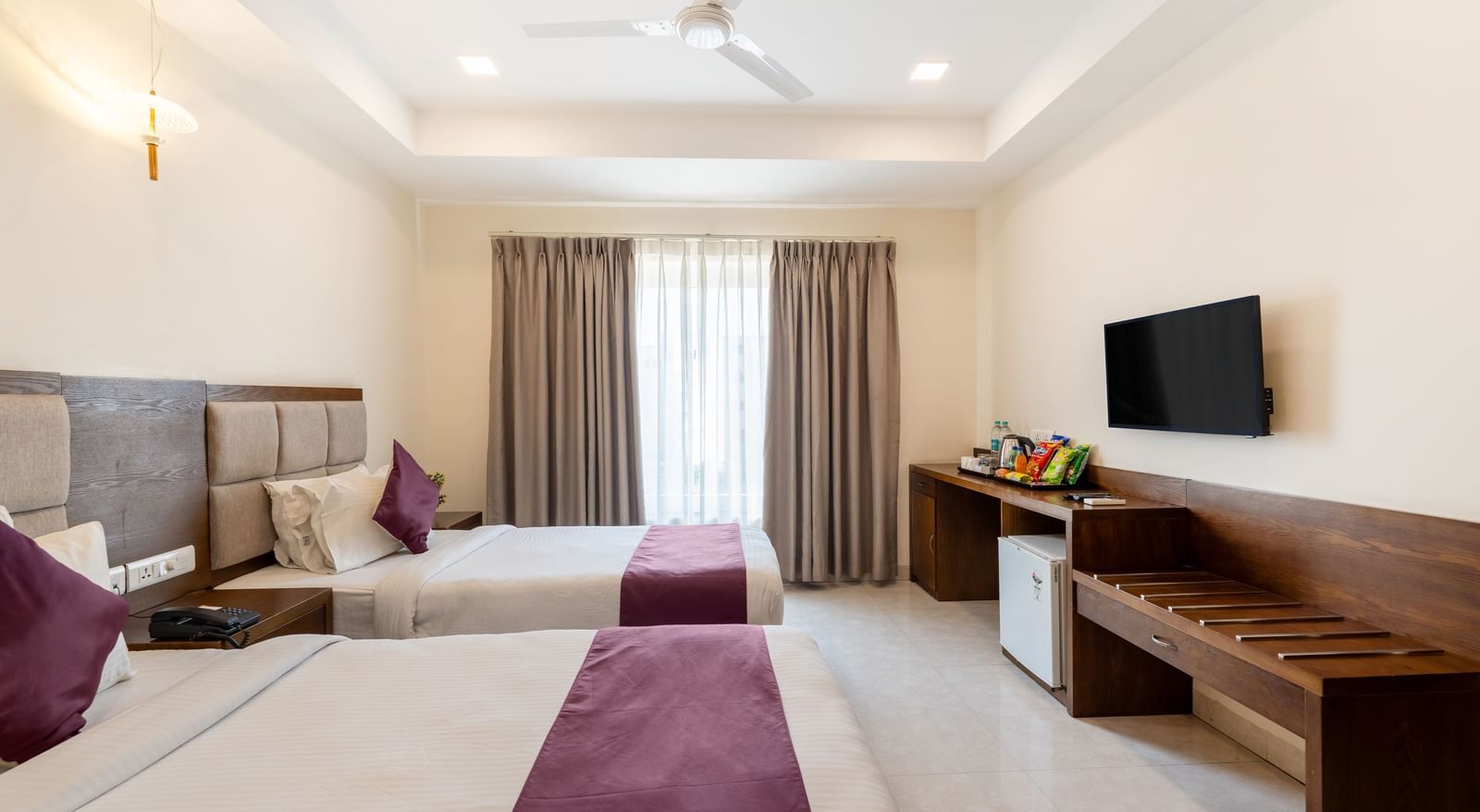 A Deluxe Room at Destino by Monday Hotels, Gachibowli, with twin beds, a work desk, a wall-mounted TV, and a large window.
