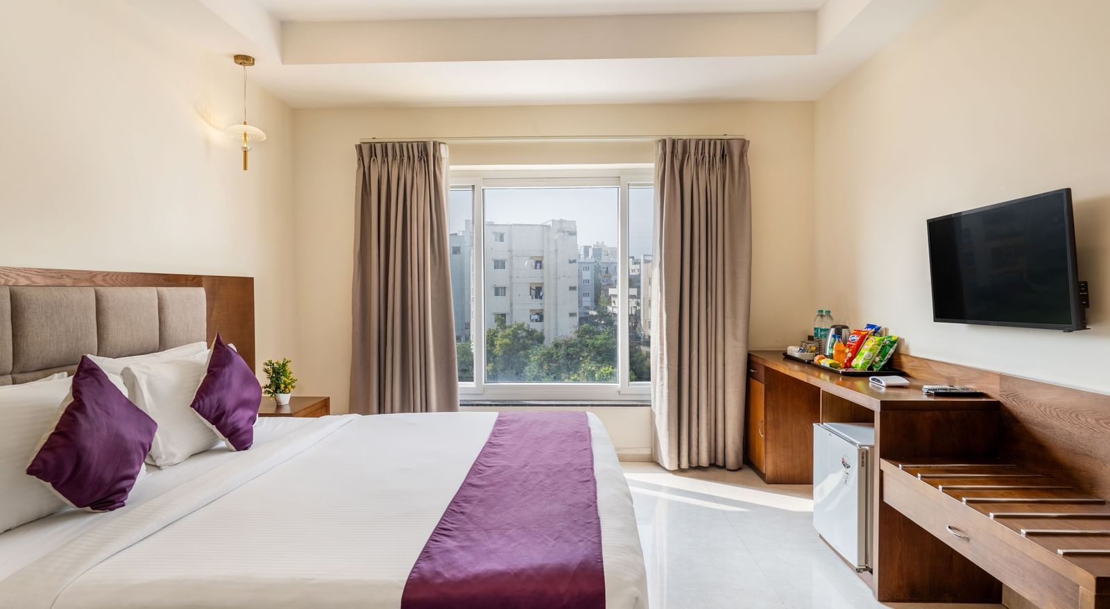 A well-lit room at Destino by Monday Hotels, Gachibowli, featuring a neatly made double bed, a wall-mounted TV, and wooden furnishings.