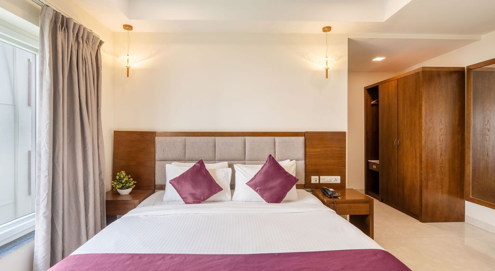 A well-lit room at Destino by Monday Hotels, Gachibowli, featuring a neatly made double bed with purple accents and a spacious wooden wardrobe.