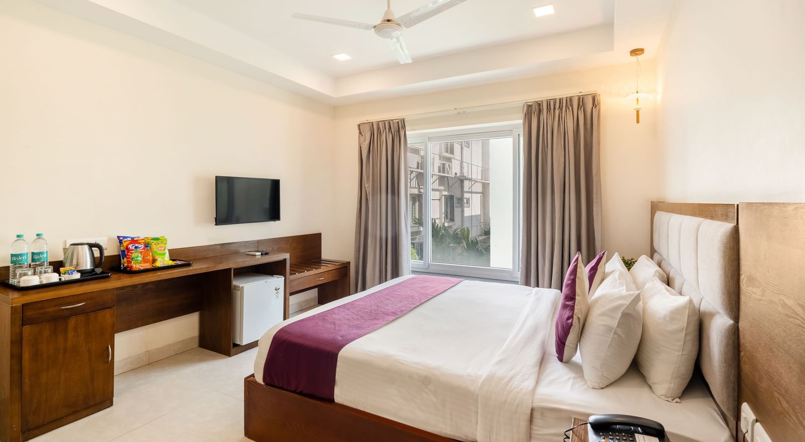 A well-lit room at Destino by Monday Hotels, Gachibowli, featuring a neatly made double bed, a wall-mounted TV, and wooden furnishings.
