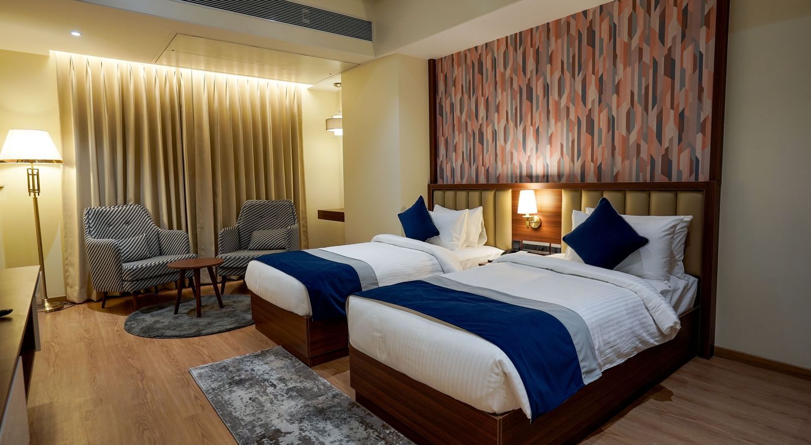 Full view shot of Superior Twin Bed Room featuring a twin bed along with 2 cushioned armchairs at the far end of the room at M2 Square by Monday Premium.