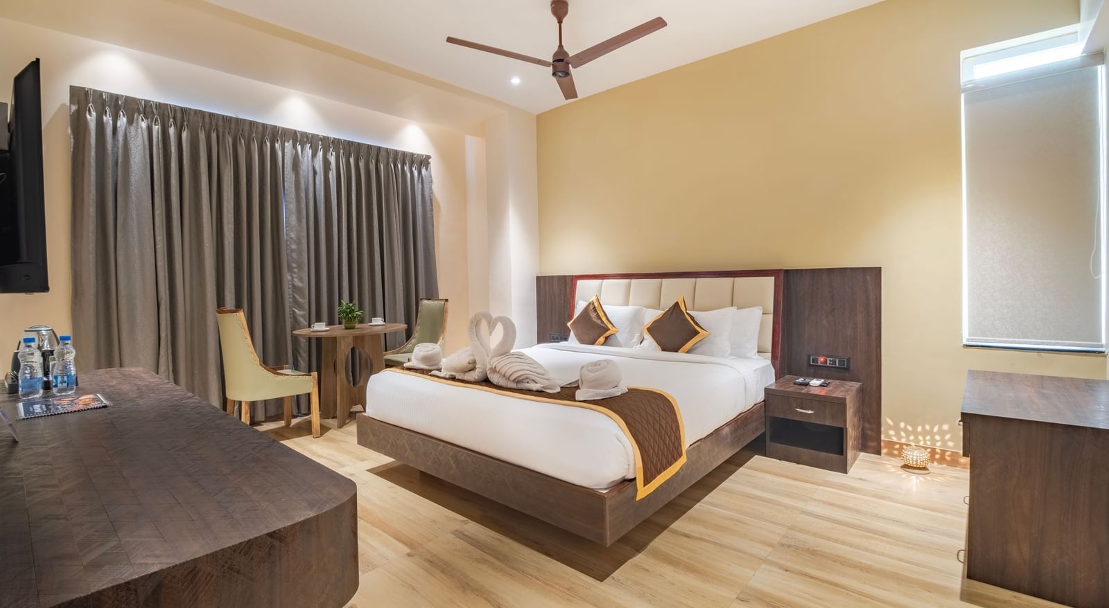 Spacious room at Monday Hotels Amalapuram Heights with warm lighting, ceiling fan, bed-side table, and a seating area.