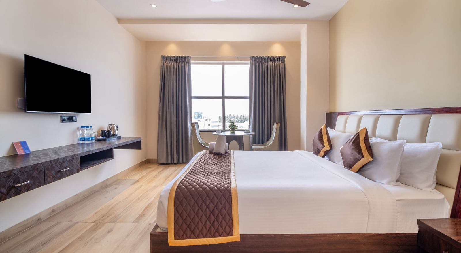Spacious room at Monday Hotels Amalapuram Heights with king size bed, TV, ceiling fan, and seating area.
