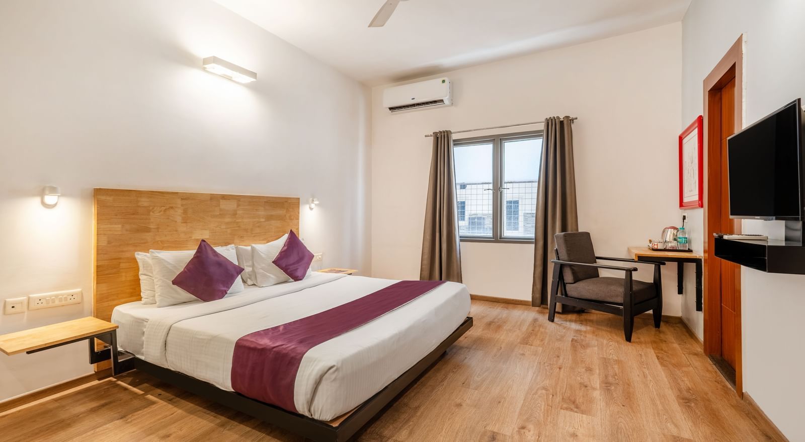 A spacious hotel room with a bed, wooden flooring, a chair and a wall mounted tv - Monday Hotels HITEC City, Hyderabad