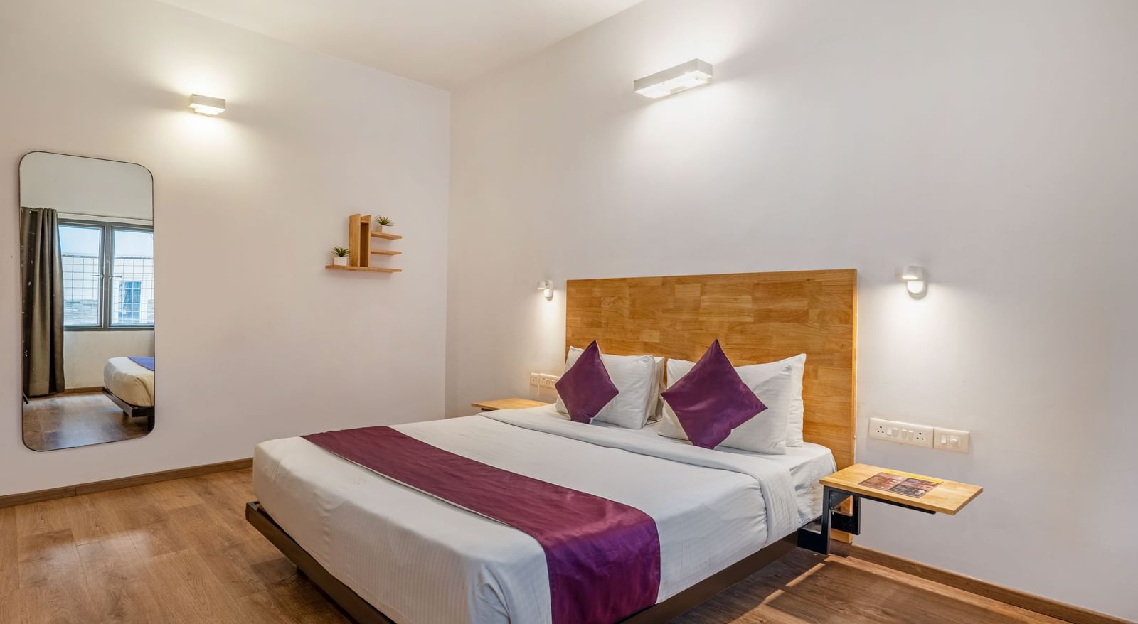 A hotel room with a double bed, wooden flooring, a large mirror and a side table - Monday Hotels HITEC City, Hyderabad