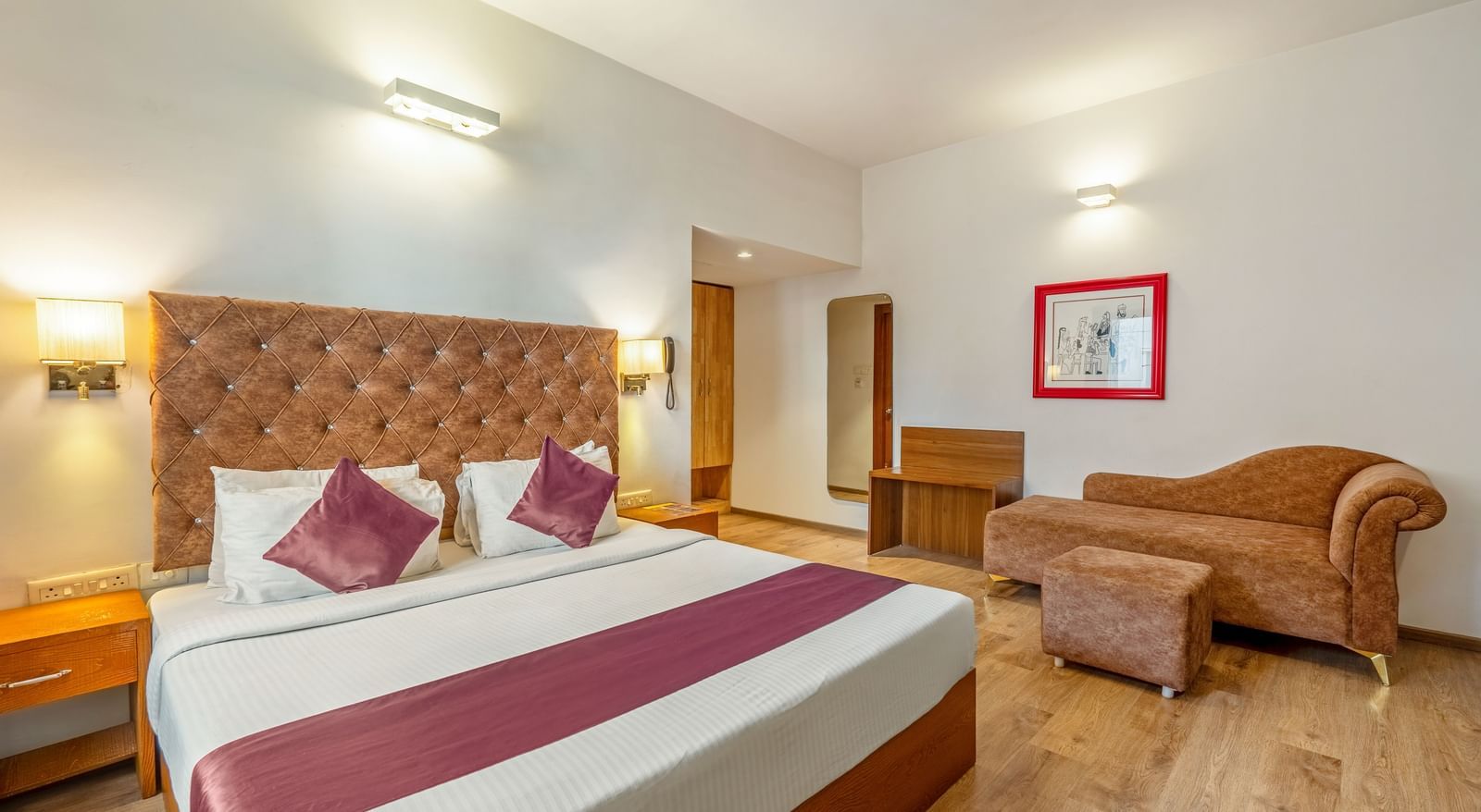 A hotel room with a double bed, a cushioned sofa, and a wooden desk placed beside the bed - Monday Hotels HITEC City, Hyderabad