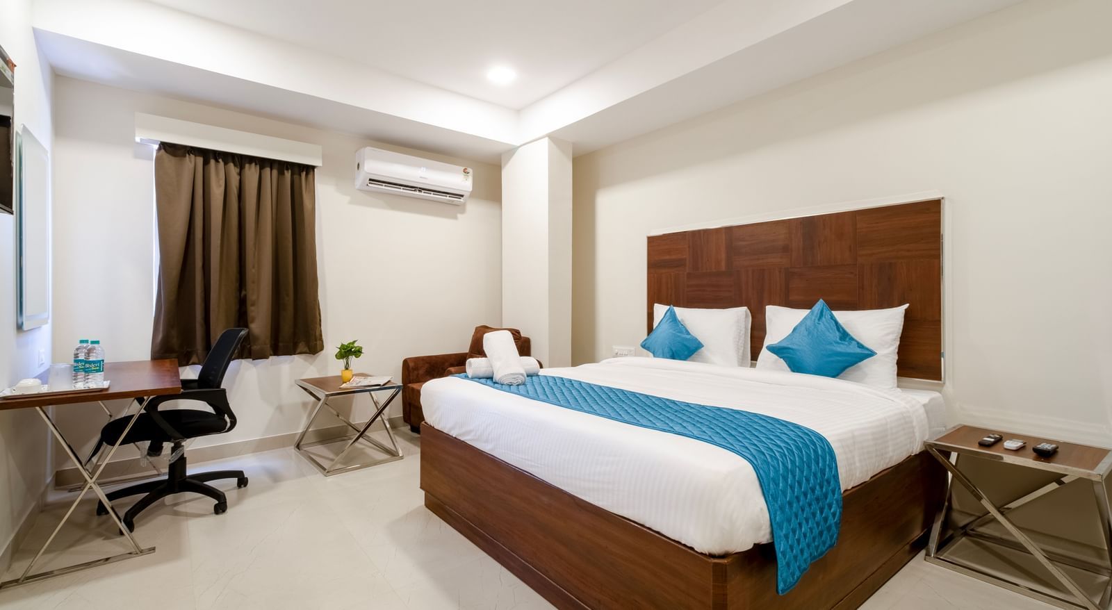 Well lit bedroom with desk comfortable chair double bed blue cushions and air-conditioning ideal for work and rest at Swarna's The Capital.