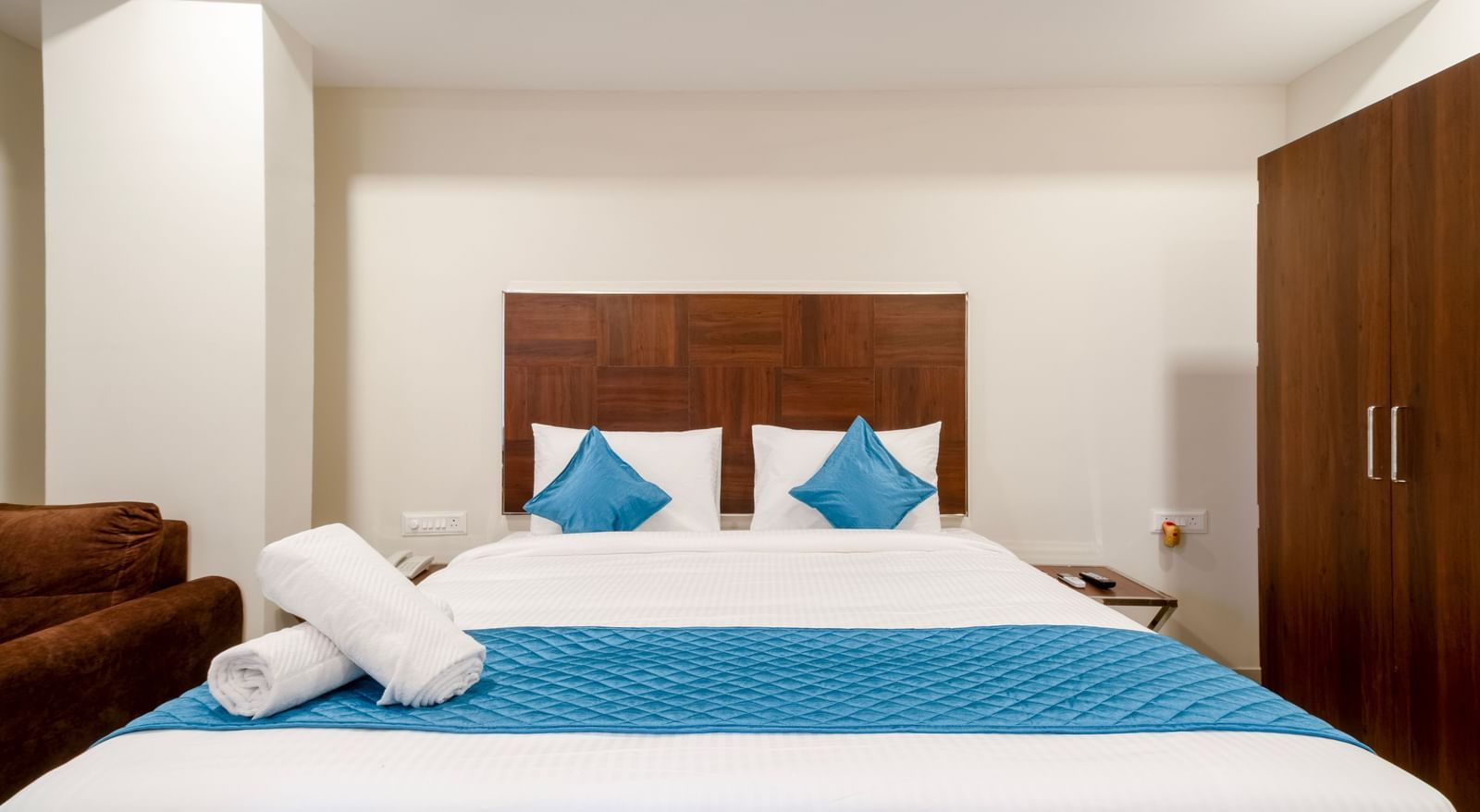 Elegant bedroom with wide bed blue accents soft pillows and wooden wardrobe offering comfort and relaxation at Swarna's The Capital.