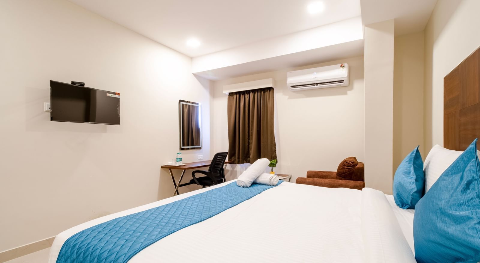 Bright bedroom with large bed blue accents television work desk seating area and air-conditioning for comfort at Swarna's The Capital.