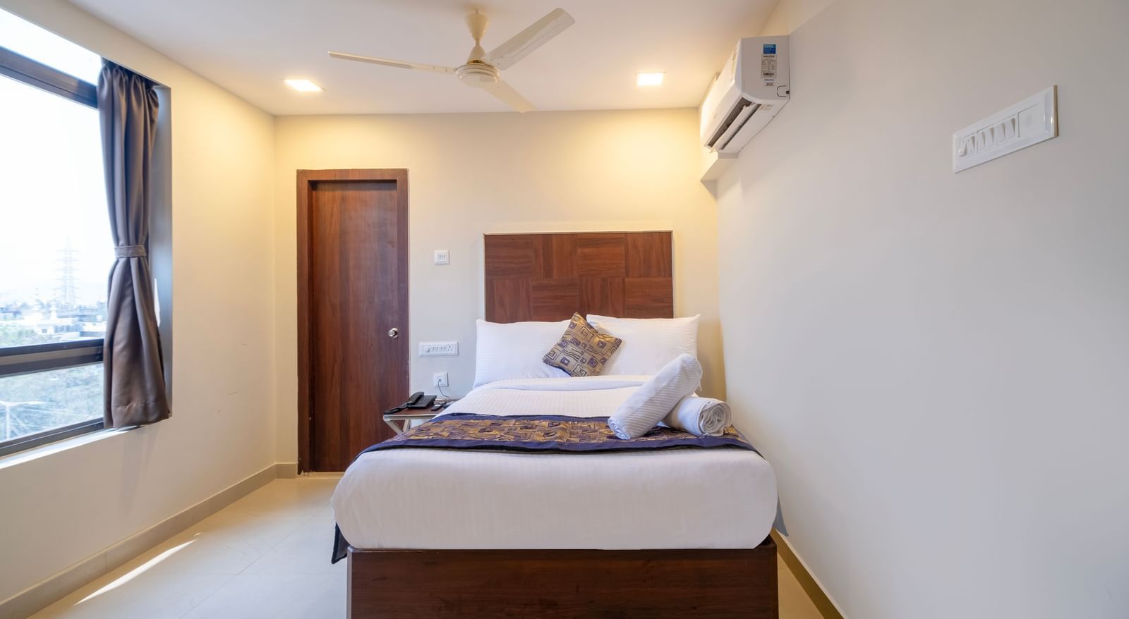 Bright bedroom with double bed soft furnishings ceiling fan air-conditioning and window for natural light at Swarna's The Capital.