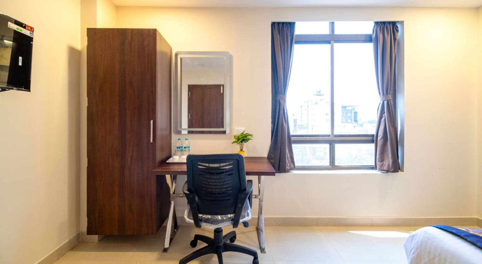 Work desk with ergonomic chair wardrobe mirror and window providing a functional and airy workspace at Swarna's The Capital.