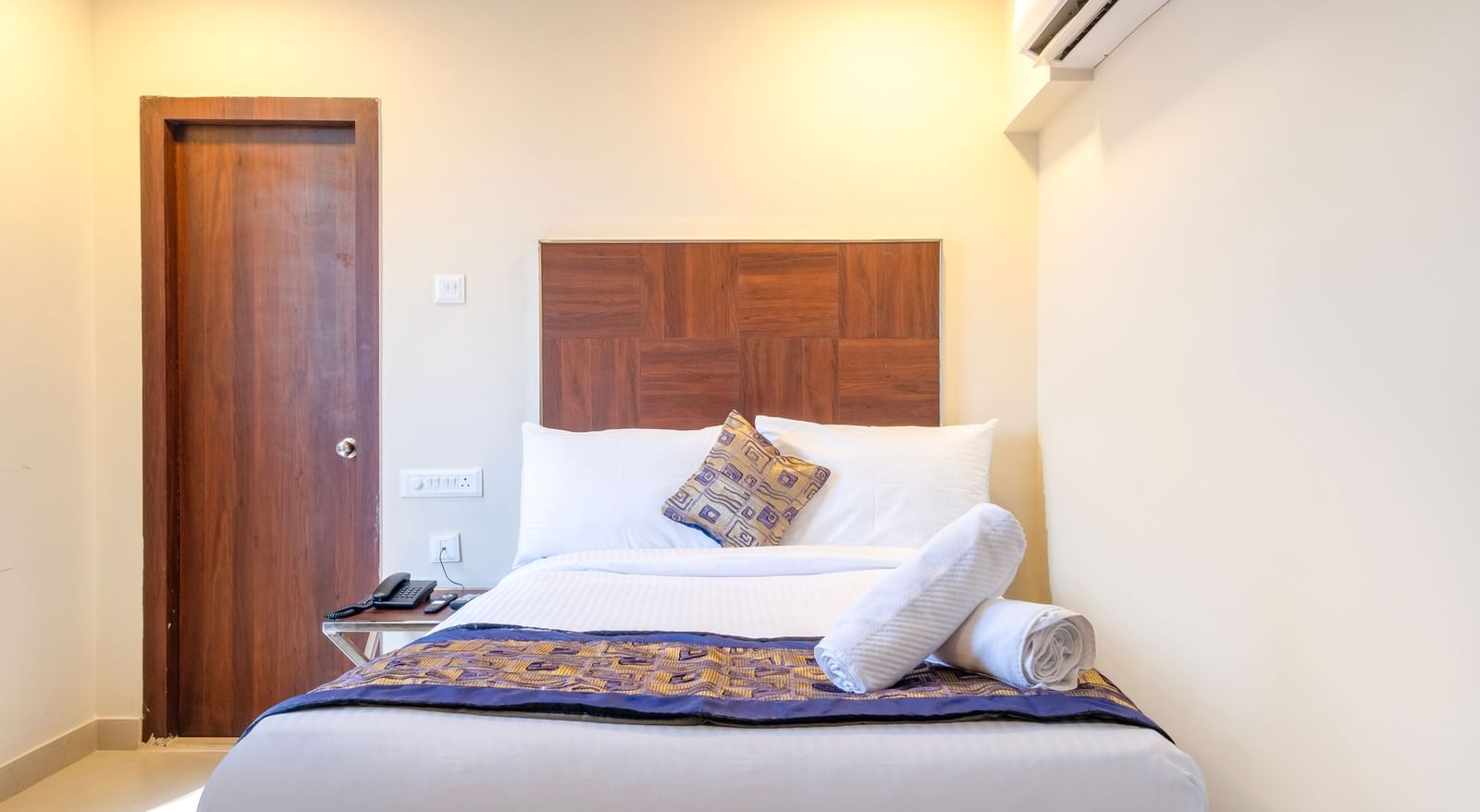 Comfortable bedroom with double bed patterned runner fresh linens and air-conditioning in a welcoming setting at Swarna's The Capital.