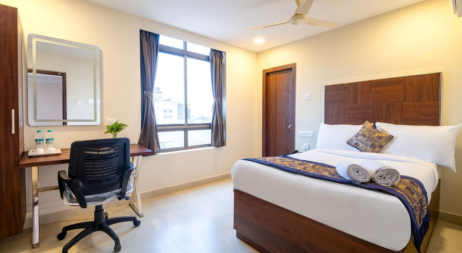 Comfortable bedroom with double bed work desk mirror chair and large window offering natural light at Swarna's The Capital.