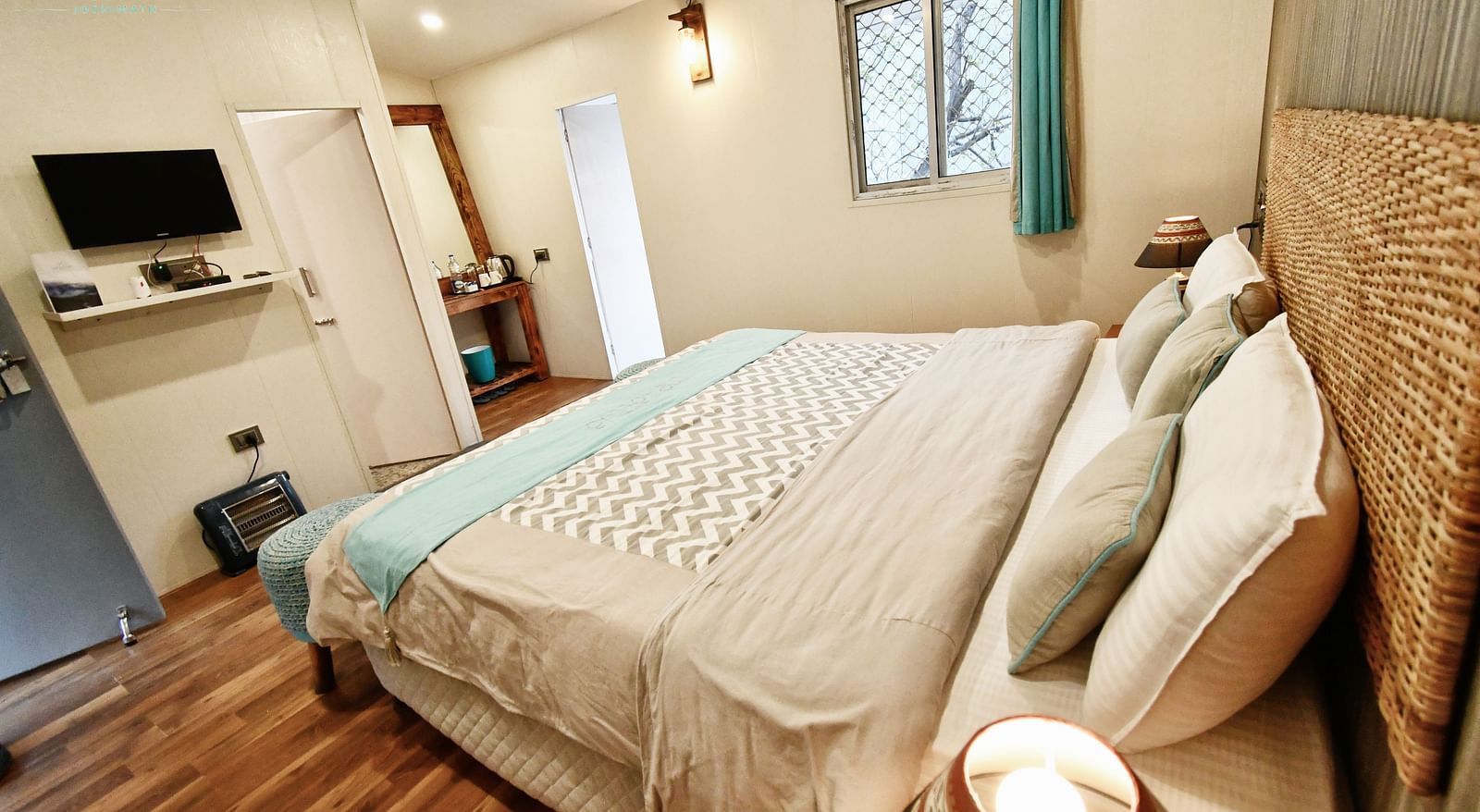 side view image of the deluxe room featuring a double bed and a wall mounted television in  front of it - The Tattva Boutique Resort