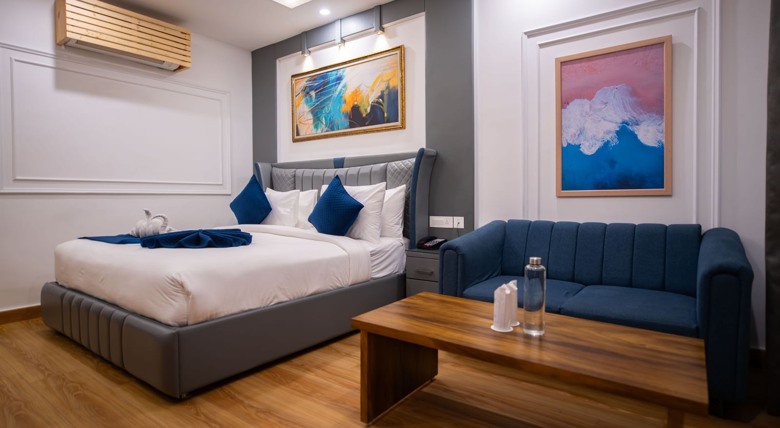  An Executive Room at The Tattva Devaprayag with a bed featuring a blue sofa and two framed paintings on the wall.