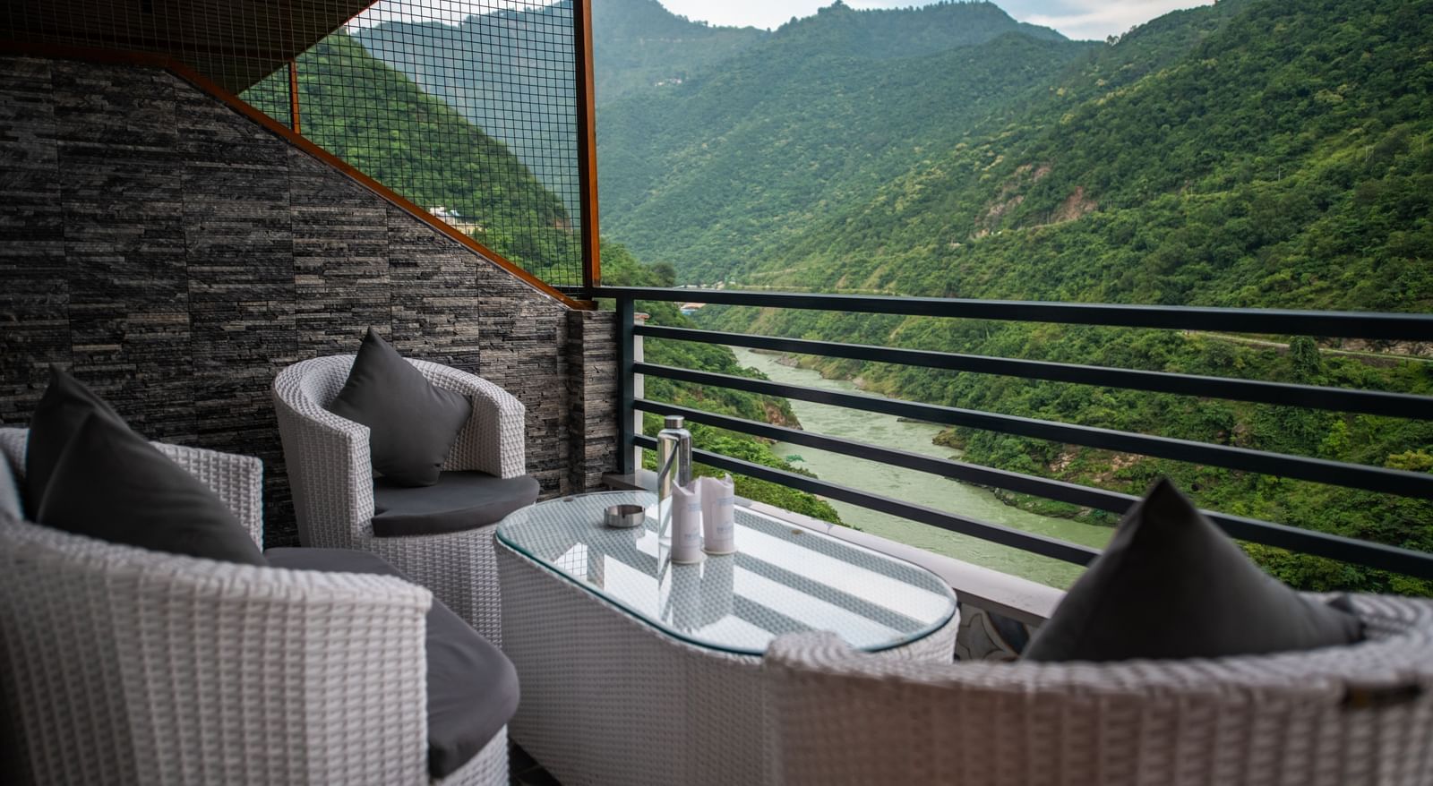 A balcony in the executive room at The Tattva Devaprayag featuring two white chairs and a table with a view of the mountains and the river.