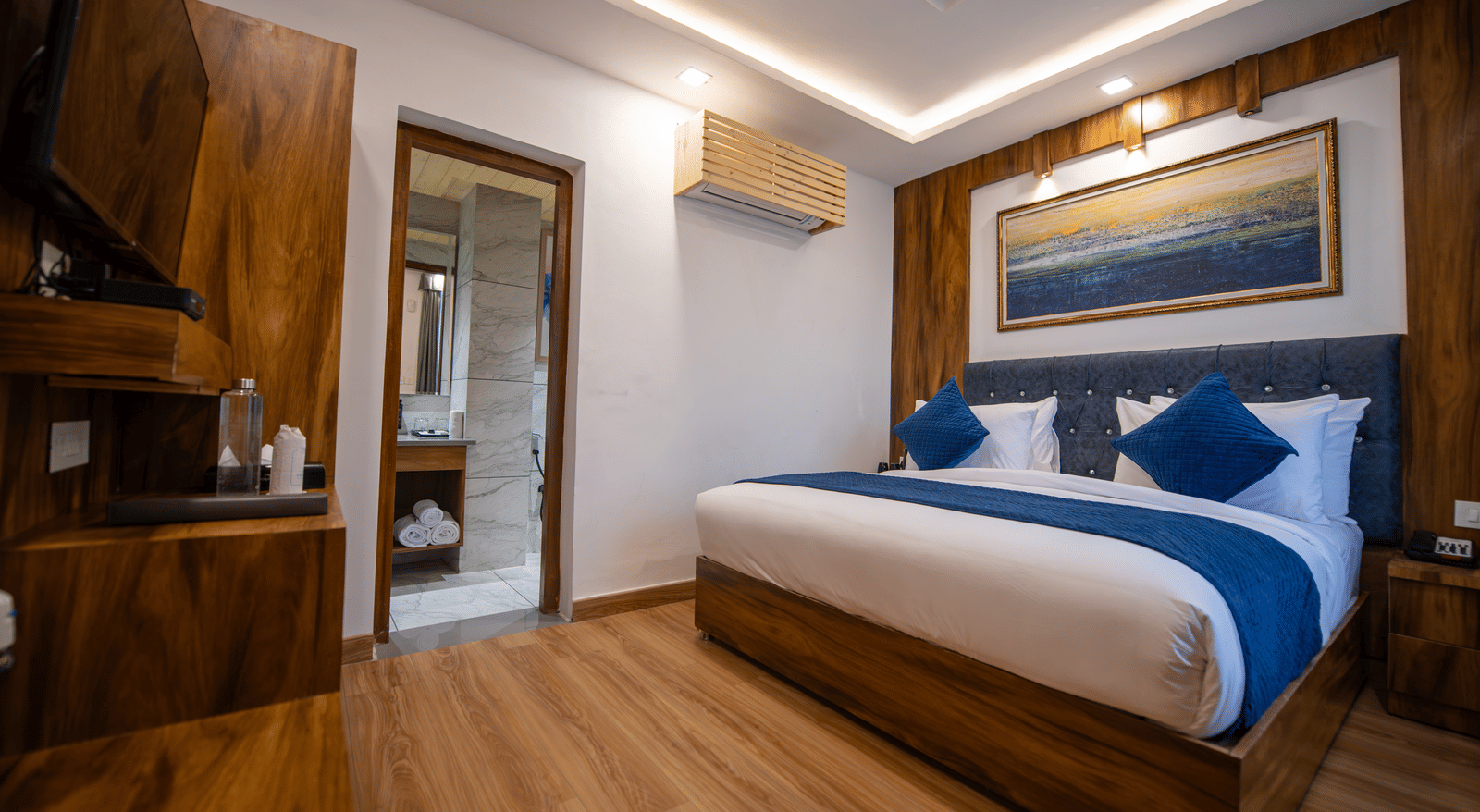 A standard room at The Tattva Devaprayag with a bed featuring blue blankets and two pillows and an open bathroom door.