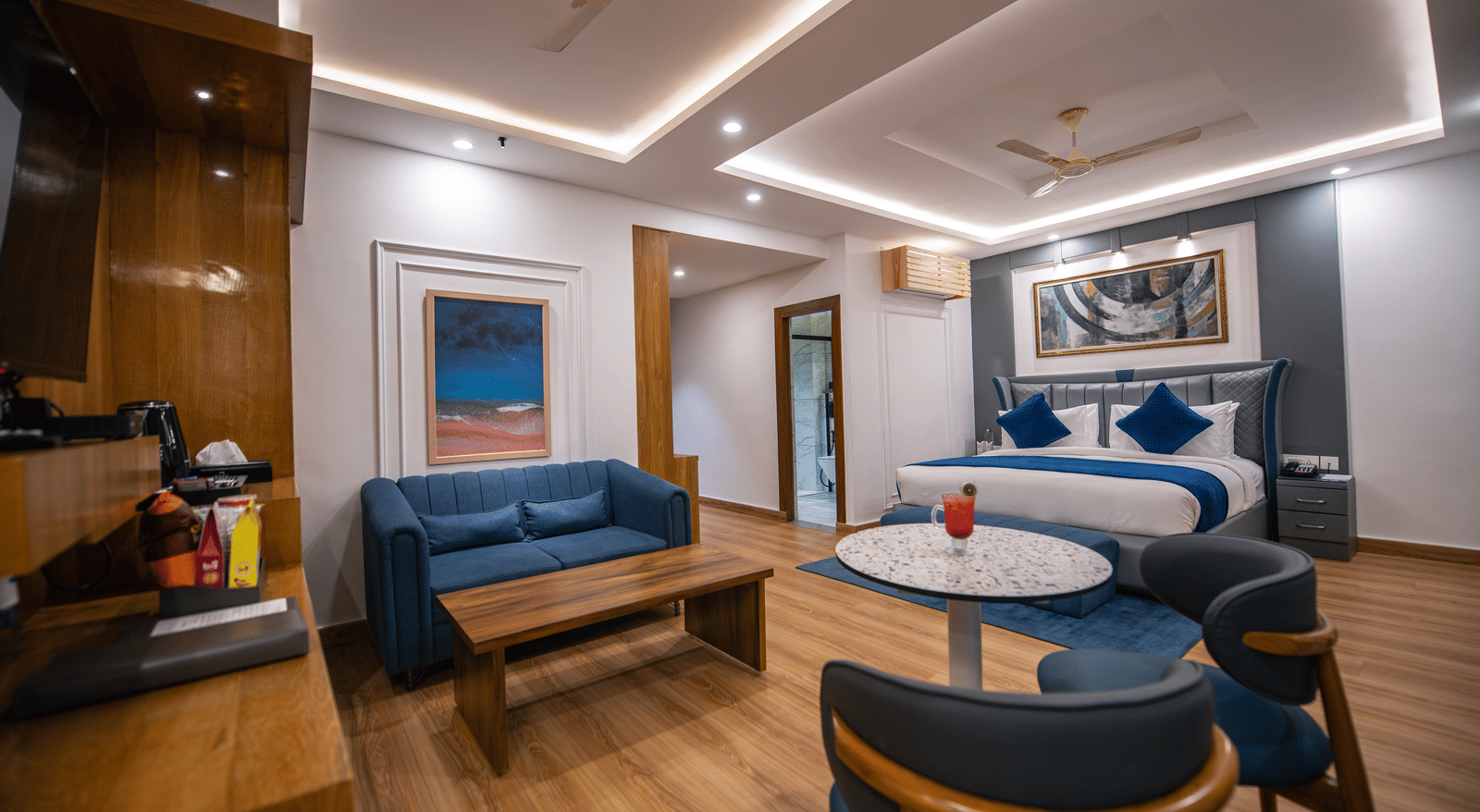 A spacious superior room at The Tattva Devaprayag with a bed featuring blue blankets, a sofa, and a round table.