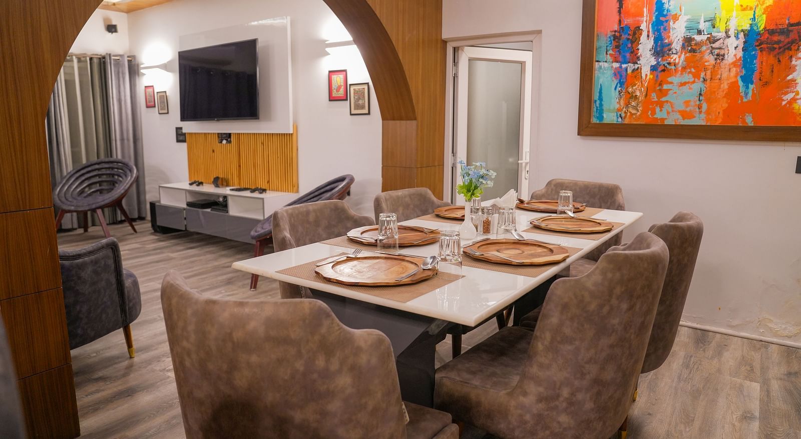 Modern dining and living room of the Pent House at The Tattva, Joshimath with neutral décor, abstract wall art, stylish furniture, and a wooden arch separating both spaces
