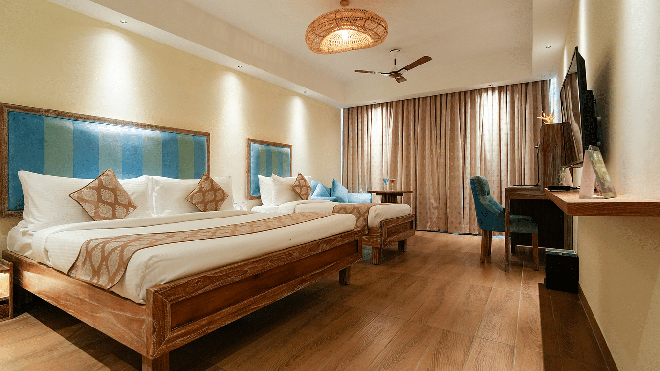 Hotel room with two beds, desk, blue chair, and window with curtains. Woven light fixture and light wood floor - MGM Beach Resorts